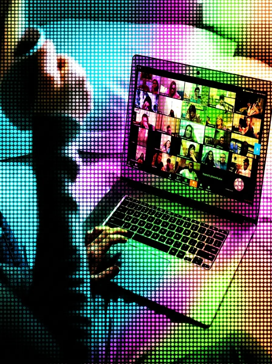 Adulto de espaldas frente a una laptop que muestra una videollamada con muchos participantes, sobre un fondo de luces multicolor.