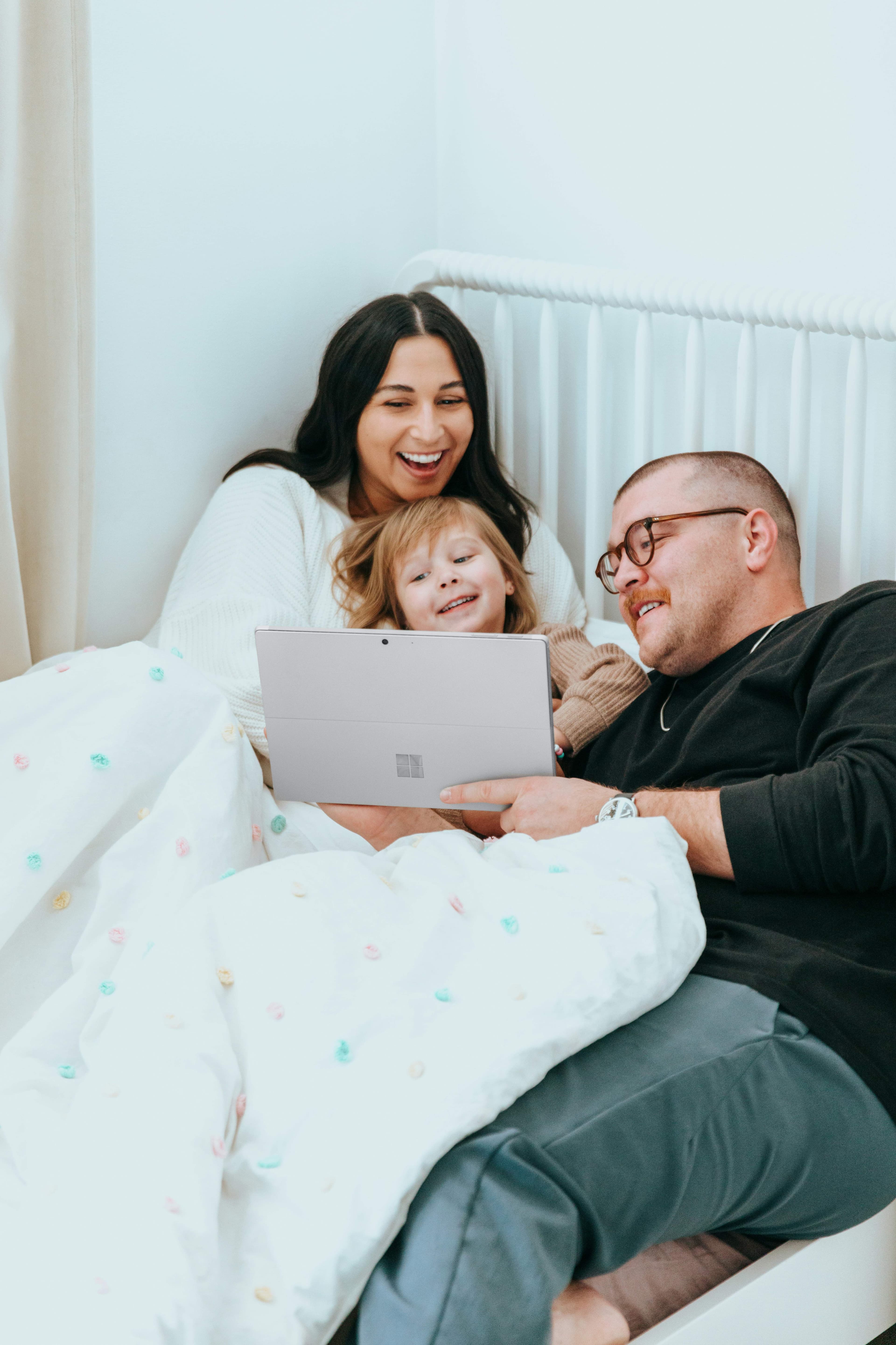 Madre, hija y padre sonríen mientras miran juntos una tableta en casa, acompañando la vida digital en familia.