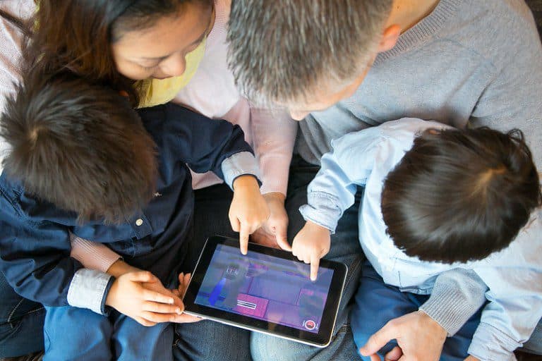Vista cenital de una familia latina que señala y explora junta la pantalla de una tableta, acompañando la vida digital en casa.