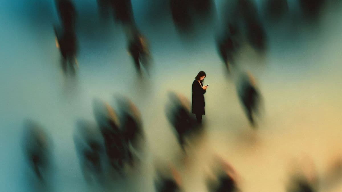 Una persona mira su teléfono, sola y quieta entre una multitud desenfocada en movimiento, evocando la soledad de la vida digital.